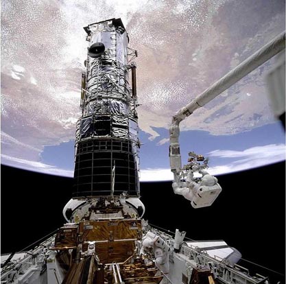 
F. Story Musgrave, anchored on the end of the Canadarm, prepares to be elevated to the top of the Hubble Space Telescope to install protective covers on the magnetometers as part of STS-61.