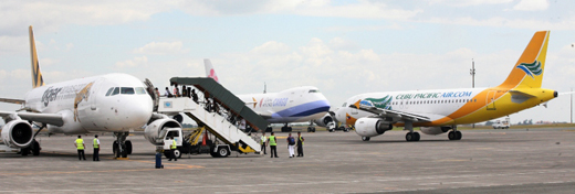 
A Cebu Pacific plane taxies between two aircraft as passengers board a Tiger Airways airplane. In the background is a China Airlines Cargo Boeing 747.