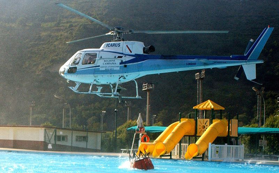 
A Eurocopter AS350 dips its bucket into a swimming pool before returning to drop the water on a wildfire outside of Naples, Italy