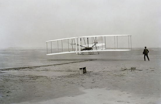 
First flight of the Wright Flyer I, December 17, 1903, Orville piloting, Wilbur running at wingtip.