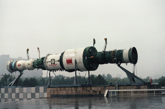 
A model of a Salyut 7 space station, with a Soyuz spacecraft and a Progress resupply spacecraft docked at each end. The display is in front of one of the pavilions of the Exhibition of Soviet National Economic Achievement